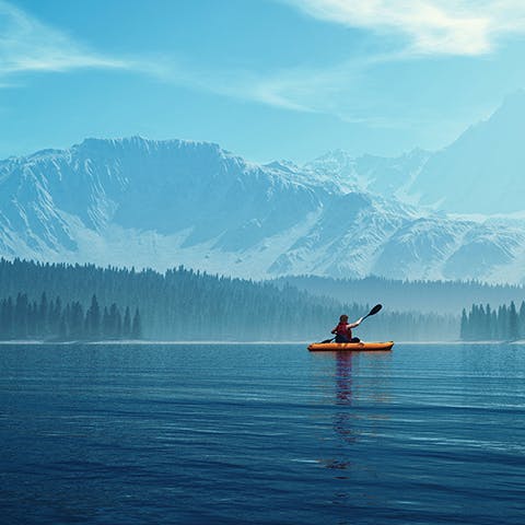 Man in a yellow canoe paddles in a lake surrounded by snow-capped mountains