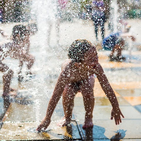 Kids play in a water fountain on a sunny day